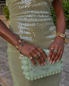 Detailed view of gold clover bracelet and malachite rings paired with a pearl handbag