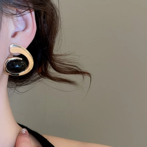 Close-up of elegant gold oval earring with black gemstone inlay worn by a model