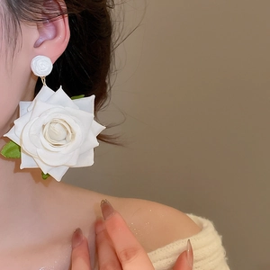 Close-up of elegant large white fabric rose earrings with green leaves worn by a model