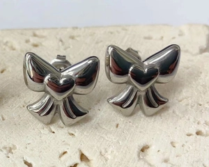 Macro shot of polished silver bow stud earrings with heart detail on a stone surface