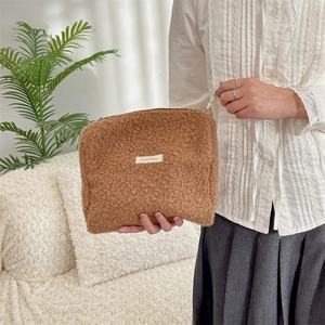 Handheld weergave van bruine teddy fleece make-up tas met rits en logo-patch detail