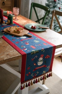 Blue festive table runner with snowman patterns and red tassels on a wooden dining table