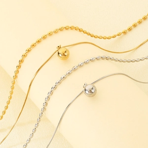 Détail de colliers en acier inoxydable doré et argenté avec pendentifs boules rondes.