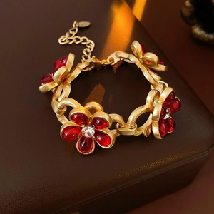 Close-up of golden vintage-style bracelet with five red glass floral charms and crystals