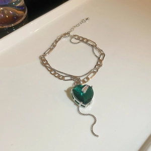 Detail of silver double-layered chain necklace with green zircon heart pendant and tassels