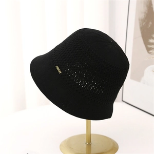 Detailed close-up of black hollow knit bucket hat with a gold metal JSHAT logo tag
