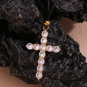 Macro detail of gold-plated cross pendant with clear zircons on black volcanic rock