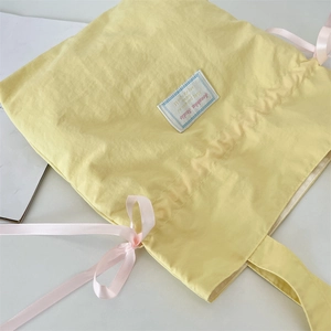 Close-up of yellow nylon tote bag featuring pink ribbon bows and aesthetic label