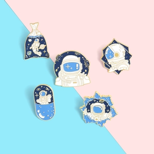 Detail view of 5 astronaut enamel pins with gold trim on pink and blue background