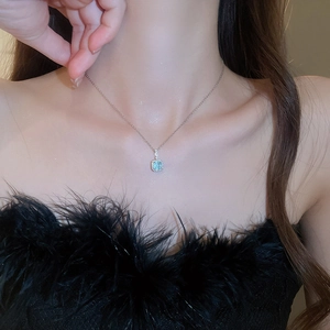 Close-up of a silver necklace featuring a square light blue pendant with a halo of small diamonds