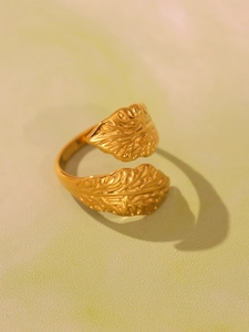 Detailed top view of gold leaf textured open ring on a soft textured background