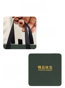 Detail of dark green jewelry gift box with gold logo and black ribbon handles