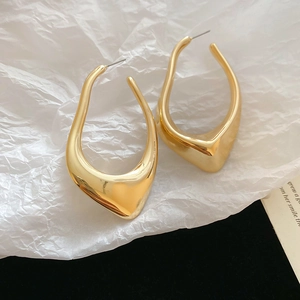 Close-up of golden irregular geometric hollow earrings on textured white paper