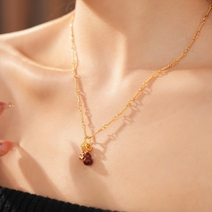 Detail of an 18k gold plated necklace featuring small red gourd-shaped beads on a model