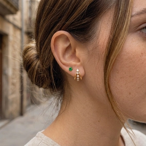 Detailed close-up of golden triple-layered C-shaped earrings with emerald stud on model