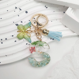 Macro detail of resin letter S keychain with real dried flowers and blue tassels