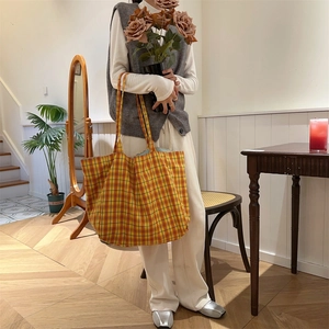 Detailed view of yellow plaid tote bag held by model in a warm indoor lifestyle setting