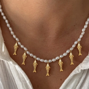 Close-up of pearl necklace with gold fish pendants worn on a neck by a model