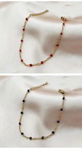 Detail of gold chain bracelets with red and black beads on silk fabric with lobster clasp