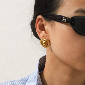 Detail of vintage gold textured round earrings with central dome on female model