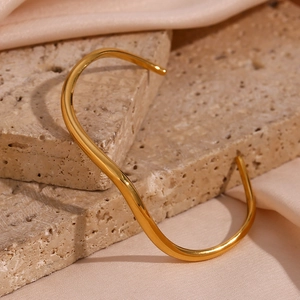 Macro shot of gold wave-shaped bangle on natural stone and pink silk fabric background