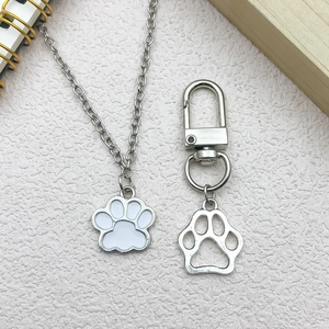 Silver cat paw pendant necklace and cutout keychain set on pink textured background