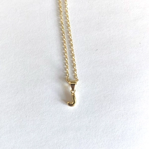 Detailed close-up of a minimalist golden necklace featuring a polished letter J pendant