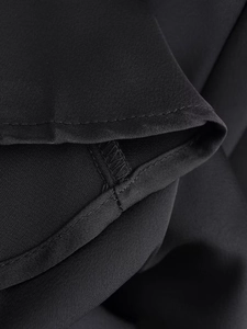 Close-up of precise stitching and hem details on black satin slip dress fabric