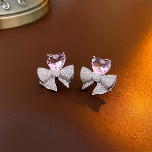 Détail de boucles d'oreilles cœur rose avec nœud en zircons sur fond en cuir