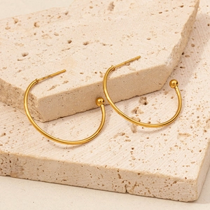 Detail of 18K gold C-shaped hoop earrings with small round ball on beige stone