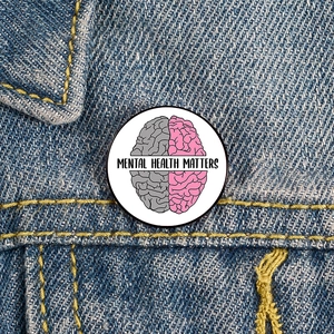 Mental Health Matters round enamel pin featuring a brain design on denim jacket background