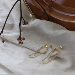 Detail of gold fringe chain earrings on linen fabric with vintage decor background