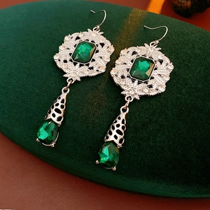 Close-up of vintage emerald green crystal drop earrings with intricate silver filigree