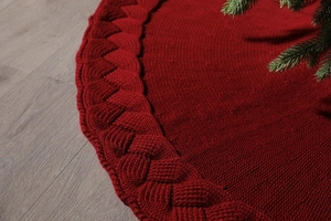 Close-up of red knitted Christmas tree skirt with thick cable knit texture on wood floor