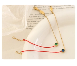 Close-up of gold-plated chain and red cord bracelet featuring a sparkling green zircon