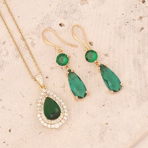 Emerald green pear-cut zircon pendant necklace and earrings set on beige stone background