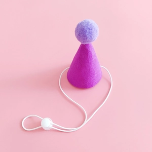Detail of purple pet birthday hat with plush ball and adjustable elastic strap