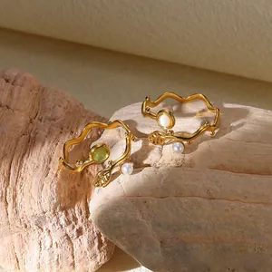 Macro detail of wave-shaped rings with pearls and green stones on natural rock texture