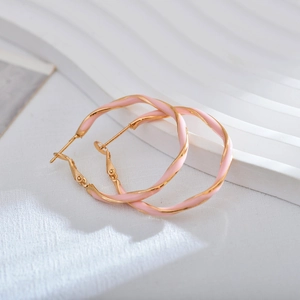 Elegant gold earrings with pink twisted enamel texture on a white textured backdrop