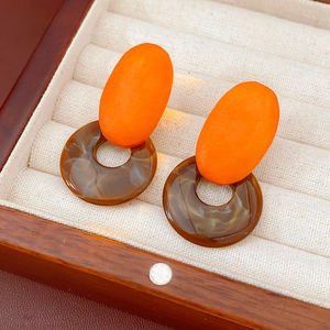Macro shot of geometric resin earrings with orange studs and amber hoops in a wooden box