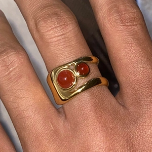 Detail of 18k gold openwork ring featuring double red agate hearts on a model's hand