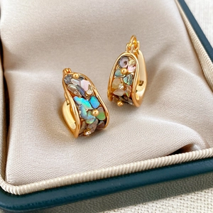 Macro shot of U-shaped gold earrings featuring colorful abalone shell and zircon stones