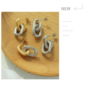 Detail of gold and silver twisted C-shape earrings displayed on a wooden tray