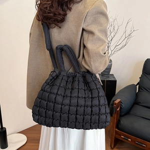 Large black quilted puffer tote bag with adjustable straps on a stylish model
