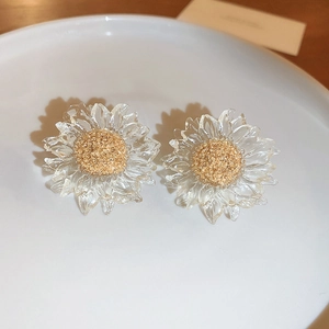 Close-up of transparent sunflower earrings with golden core on a white ceramic plate