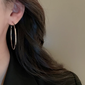 Close-up of minimalist silver geometric hoop earrings worn by a model on a grey background