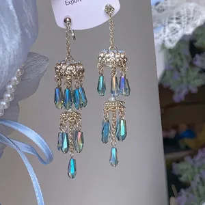 Détail de boucles d'oreilles à pompons dorés avec cristaux et strass brillants