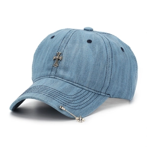 Detail of light blue denim baseball cap featuring vintage silver metal cross and pin pendant