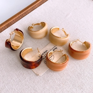 Détail de boucles d'oreilles en résine en forme de C, écaille et beige sur tissu beige