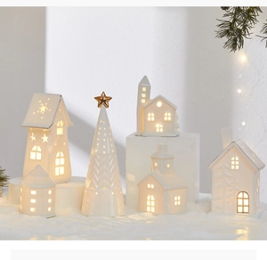 Close-up of white ceramic LED Christmas tree and house ornaments with warm glow